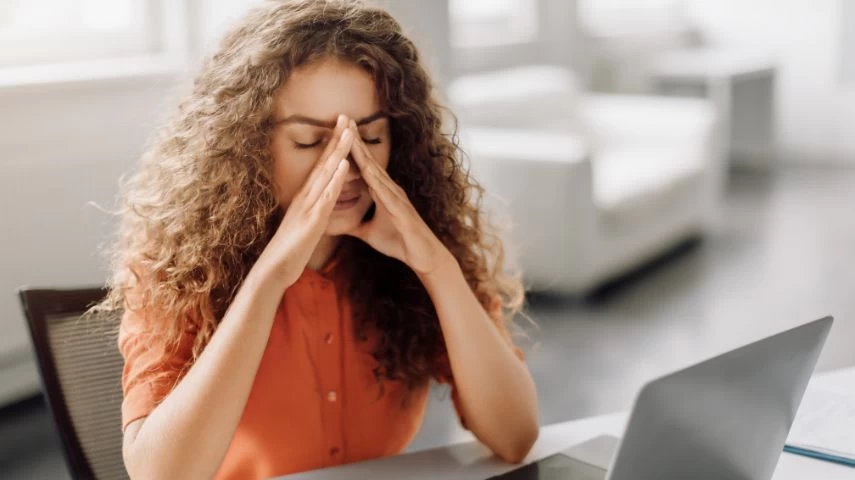 Devojka sedi ispred laptopa i žmuri zbog zamora očiju.